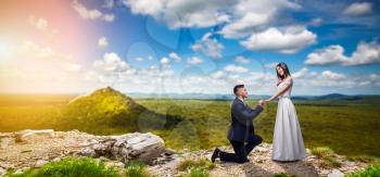 Groom makes the bride a marriage proposal, love couple in an unusual place, green valley on background. Newlywed, newly married couple