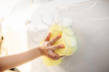 Young woman with sponge scrubbing vehicle with foam, car wash. Lady on self-service automobile washing. Outdoor carwash at summer day