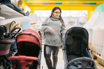 Pregnant woman in shop of goods for newborns. Future mother choosing stroller for her child