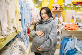 Pregnant woman buying clothes in the store for newborns. Future mother in shop of goods for infants