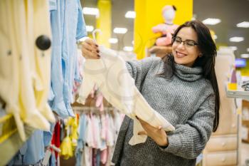 Happy future mother choosing clothes in the store for newborns. Pregnant woman in shop of goods for infants