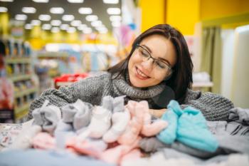 Cheerful future mother in glasses buys baby clothes in the store for newborns. Pregnant woman in shop of goods for infants