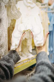 Female person chooses baby clothes in the store for newborns. Pregnant woman in shop of goods for infants