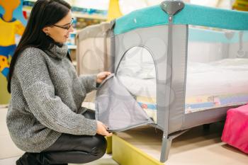 Pregnant woman buying cot in store. Future mother in shop of goods for newburns