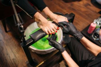 Pedicurist in black gloves doing cosmetic procedure with pedicure bath, female client in beauty salon. Professional  fingernail care, feet massage