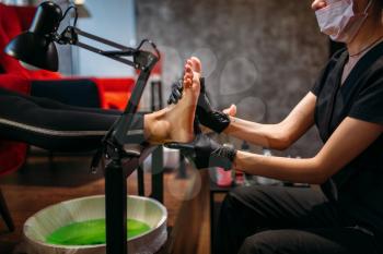 Pedicurist in black gloves rubs the cream, female client in beauty salon.  Professional  fingernail care, feet massage after pedicure bath, podiatry procedure