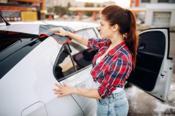 Woman wipes the car with a cloth after washing, polishing process on self-service car-wash. Lady cleaning vehicle