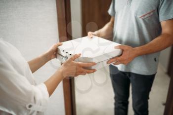Pizza delivery man gives carton box to female client at the door, delivering service. Courier from pizzeria and woman indoors, takeaway deliver