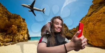 Nice female sportman windsurfer in wetsuit with phone on the beach, monkey sitting on her shoulder, plane flying on background