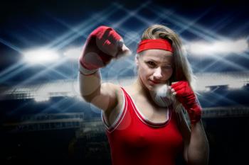 Female kickboxer in red boxing bandages makes punchagainst lights. Fighting sport concept