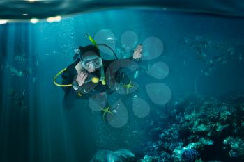 Diver in wetsuit and diving gear speaks on phone, underwater view. Frogman in mask and scuba swims in the ocean