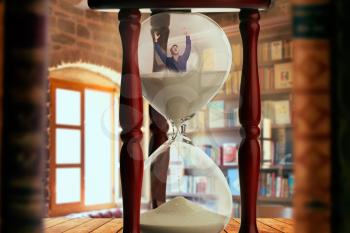 Man drowning inside an hourglass, deadline concept, bookshelf in the office on background