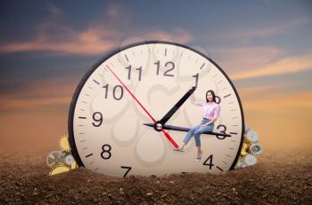 Young woman sitting on the arrow of a huge clock. Deadline concept, time does not stop