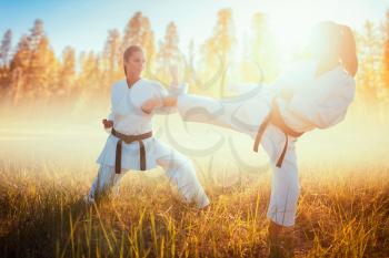 Two female karate in kimono fight in summer field. Martial art fighters on workout outdoor, technique practice
