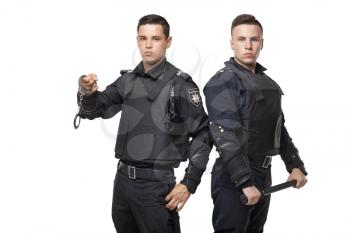 Special force troops with a baton and handcuffs, black uniform and body armor, white background. Two armed police officers in special ammunition