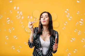 Beautiful woman with soap bubble, yellow background. Female person blowing colorful balloons
