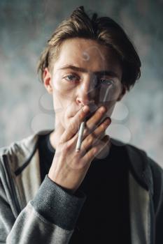 Young man smoke cigarette, grunge background. Addiction concept, smoking drugs
