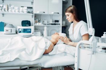 Beautician makes face massage to female patient, cosmetology clinic. Facial skincare, rejuvenation procedure in spa salon