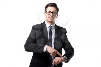 Young businessman in glasses, tie and black suit point a finger on the watch, isolated on white background