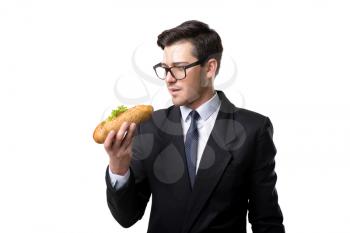 Young businessman in glasses, tie and black suit eats burger, isolated on white background