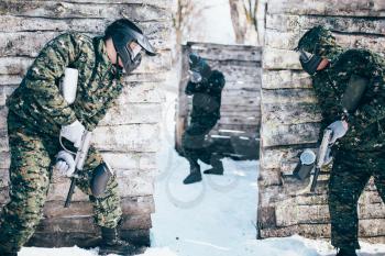 Paintball battle, paintballing, team shooting in winter forest. Extreme sport, active military game