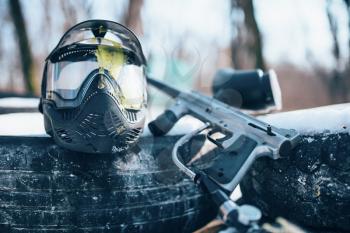 Splattered paintball mask with glasses and marker gun closeup, nobody. Extreme game equipment, sport ammunition