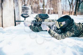 Two paintball players lies on the snow and shooting at the enemy in winter forest battle. Extreme sport game