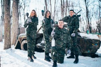 Paintball team in uniform and masks poses with marker guns in hands after winter forest battle. Extreme sport game