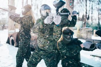 Paintball players in uniform and masks poses with marker guns in hands after winter forest battle. Extreme sport game