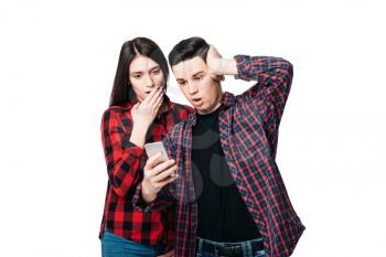 Phone addiction, surprised couple looks on smartphone screen, white background. Consciousness manipulation concept