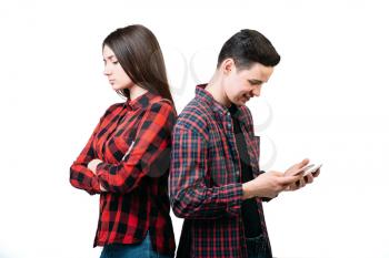 Smartphone addicted people. Couple standing back to back, man using mobile phone, white background. Manipulation of consciousness concept