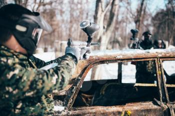 Paintball battle, players shoots because of burned car in winter forest, paintballing. Extreme sport, military game