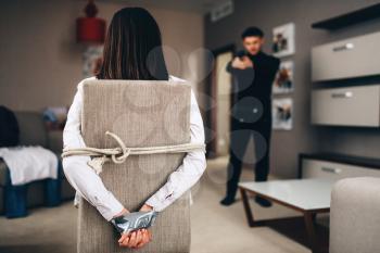 Robber in black clothes put the gun to the temple of his female victim tied with rope and tape to the chair. Robbery at home, maniac penetrated the apartment