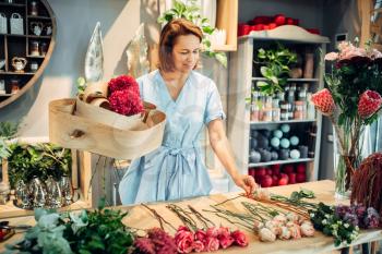 Female florist decorates composition with birch bark on the table in flower shop. Floral artist making bouquet at the workplace