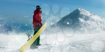 Snowboarder holds board in hands, blue sky and snowy mountains on background. Winter active sport, extreme lifestyle, snowboarding