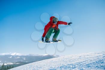 Snowboarder makes a jump on speed slope, sportsman in action. Winter active sport, extreme lifestyle. Snowboarding in mountains, blue sky on background