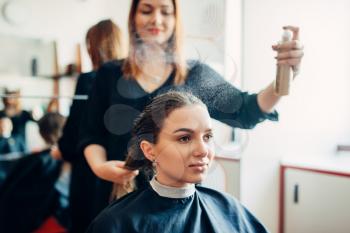 Hairdresser works with hair spray, female client in hairdressing salon. Hairstyle making in beauty studio