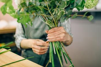 Female florist in apron holds flower composition in hand, fresh bouquet preparation process. Floral business owner at workplace