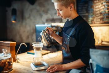 Male barista pours ground coffee into the glass standing on the stove. Barman works in cafeteria, bartender occupation