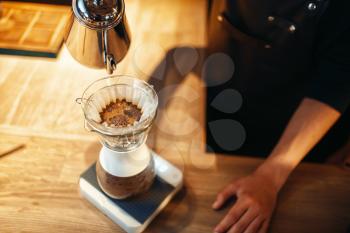 Male barista pours hot water into the glass, latte preparation, wooden cafe counter on background. Barman works in cafeteria, bartender makes coffee