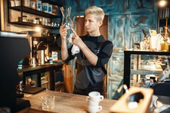 Young male barista checks clean dishes after making coffee at cafe counter. Barman works in cafeteria, bartender occupation