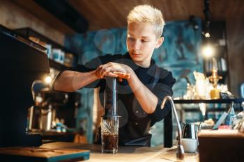 Young male barista makes fresh espresso, black coffee preparation at cafe counter. Barman works in cafeteria, bartender occupation