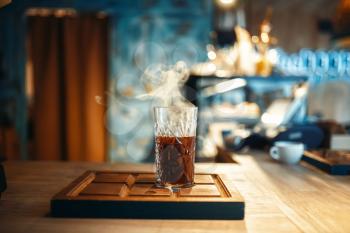 Glass of fresh hot black coffee stands on wooden counter in espresso cafe, side view, cafeteria interior on background, nobody