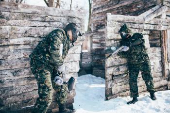 Paintball battle, paintballing, team shooting in winter forest. Extreme sport, active military game