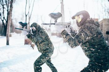Paintball team in uniform attack in winter battle. Extreme sport game, soldiers in protection masks and camouflage holds weapon in hands