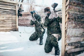 Paintball team, players in winter battle. Extreme sport game, soldiers in protection masks and camouflage holds weapon in hands