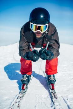 Skier in helmet and glasses racing from the mountain, front view. Winter active sport, extreme lifestyle. Downhill skiing