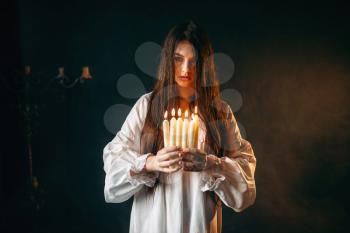 Female person in white shirt holds candles in hands. Dark magic ritual, occultism and exorcism, divination