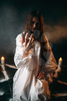 Witch in white shirt calls upon the spirits, pentagram circle with candles, dark magic ritual process, witchcraft. Occultism and exorcism