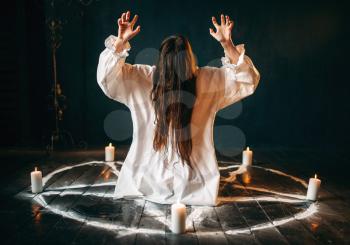 Witch in white shirt produses occult ritual in pentagram circle with candles. Dark magic ritual, occultism and exorcism